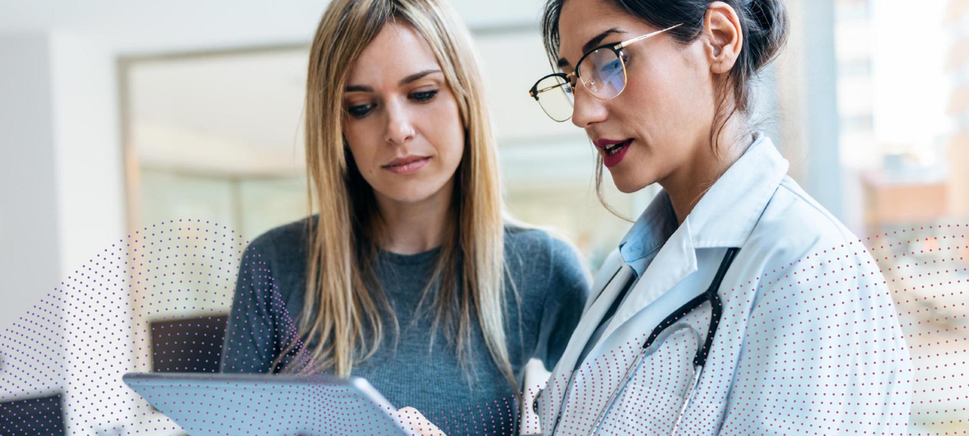 Two women are standing up looking at a screen on a tablet.