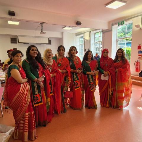 A group of 8 Bengali ladies all dressed in traditional red dress are standing together for a photo