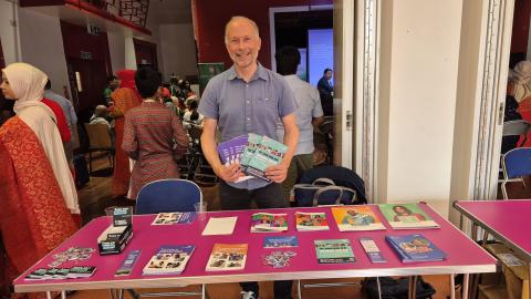 A man is standing behind a table which has cancer information leaflets on it.