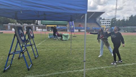 A couple of females are trying axe throwing at a target under a gazebo in a field.
