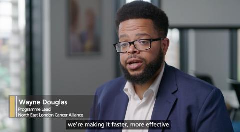 A man wearing a suit and glasses is talking in front of a camera.