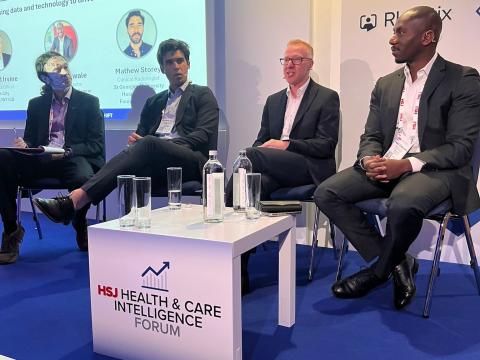Four men are sitting on a stage doing a panel discussion at the HSJ Health and Care Intelligence Forum.