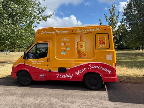 An ice cream van is stationary in a park and has been repainted in bright yellow. Instead of advertising ice cream it is promoting sun cream.