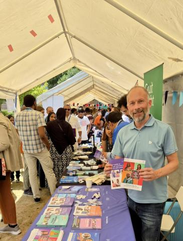 A man is standing behind a table holding a couple of leaflets which have cancer information in them.