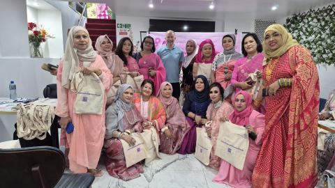 A man in a blue shirt in in the middle of a large group of asian ladies wearing pink outfits