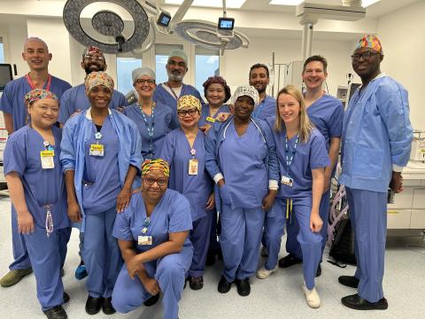 A team of clinicians in hospital scrubs is standing in a hospital operating theatre for a team photo.