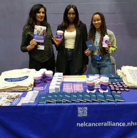 Three women are standing behind a table which has information about HPV on it.