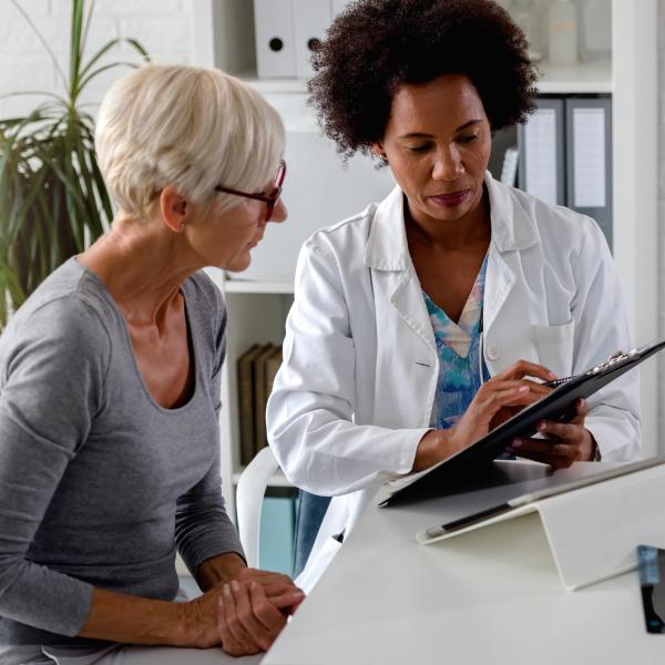 A lady with white hair and glasses is talking to a healthcare professional wearing a white jacket