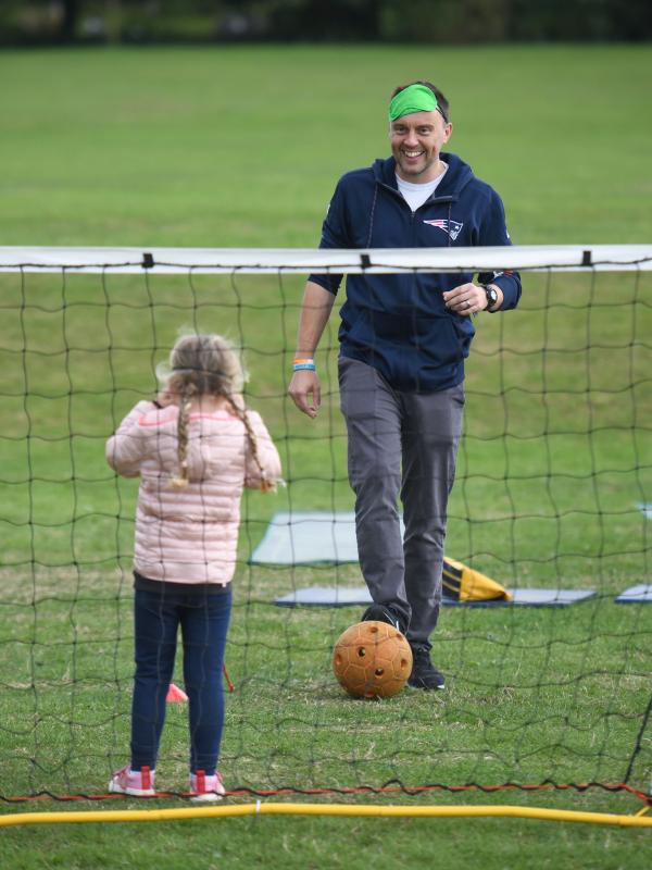 A father is kicking a football towards his daughter who is standing in a goal.
