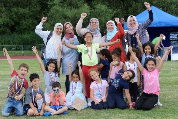 A large group of women and children are wearing medals and celebrating with their hands in the air.