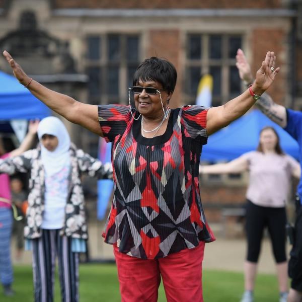 A lady is taking part in an exercise class with her arms stretched out in the air in front of a group of people.