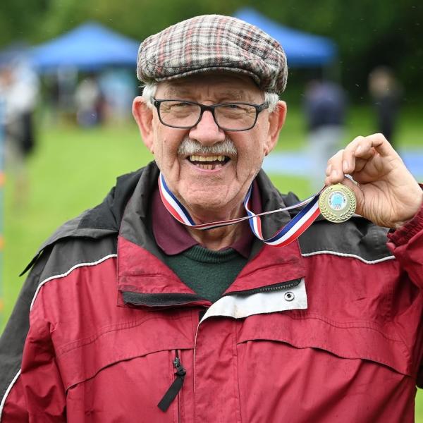 An old man wearing a cap and sports jacket is wearing a meal and holding it up in his hand.