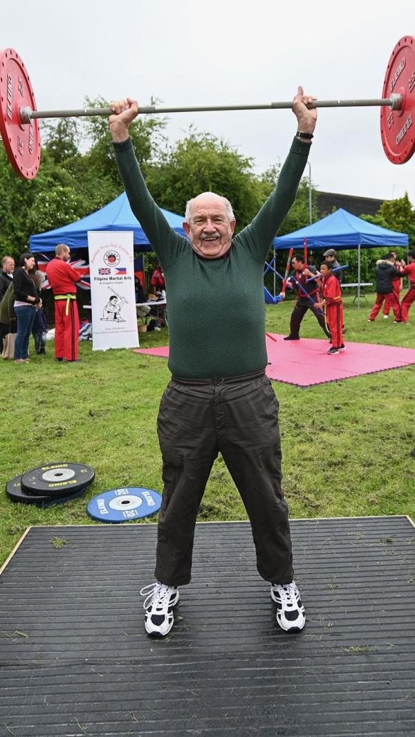 An old man is lifting a set of weights in a park.