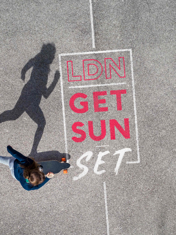 A skater is skating on concrete. On the concrete are the words LDN Get Sun Set.